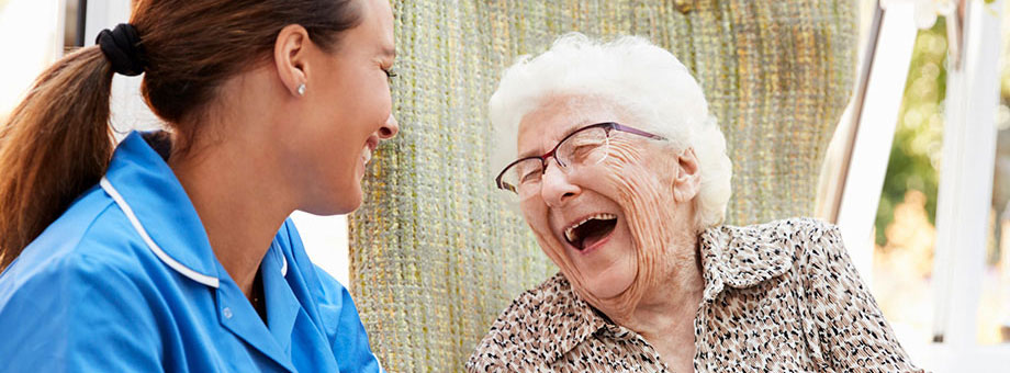 An elderly woman laughs and smiles with a health care professional