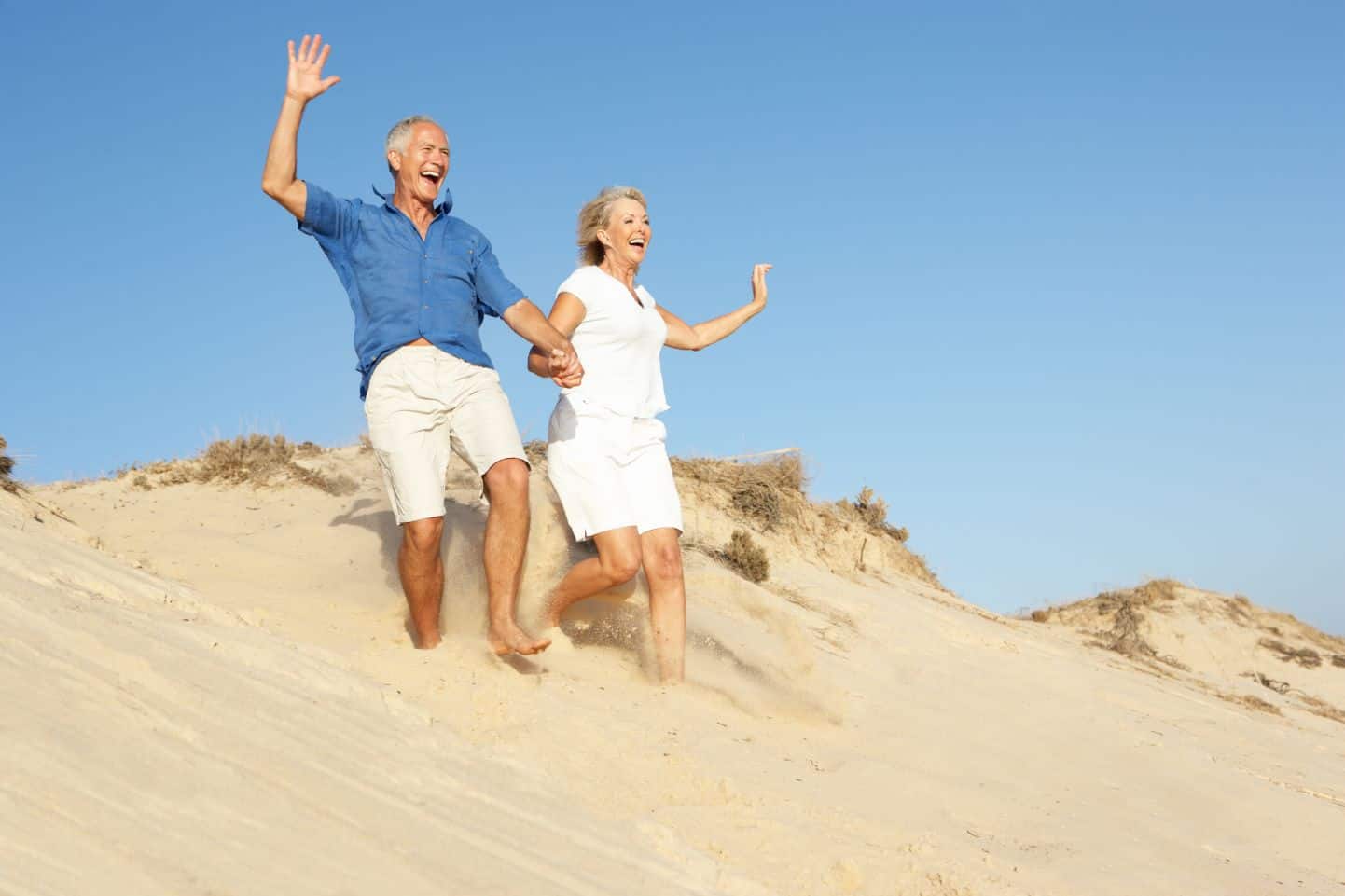 A senior couple experiences old age and independence by running in the sand.
