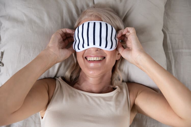 Smiling senior woman putting on an eye mask before bed to sleep better.