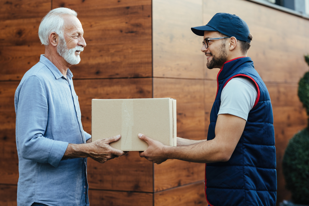 A senior man hands a sealed box or package to a man