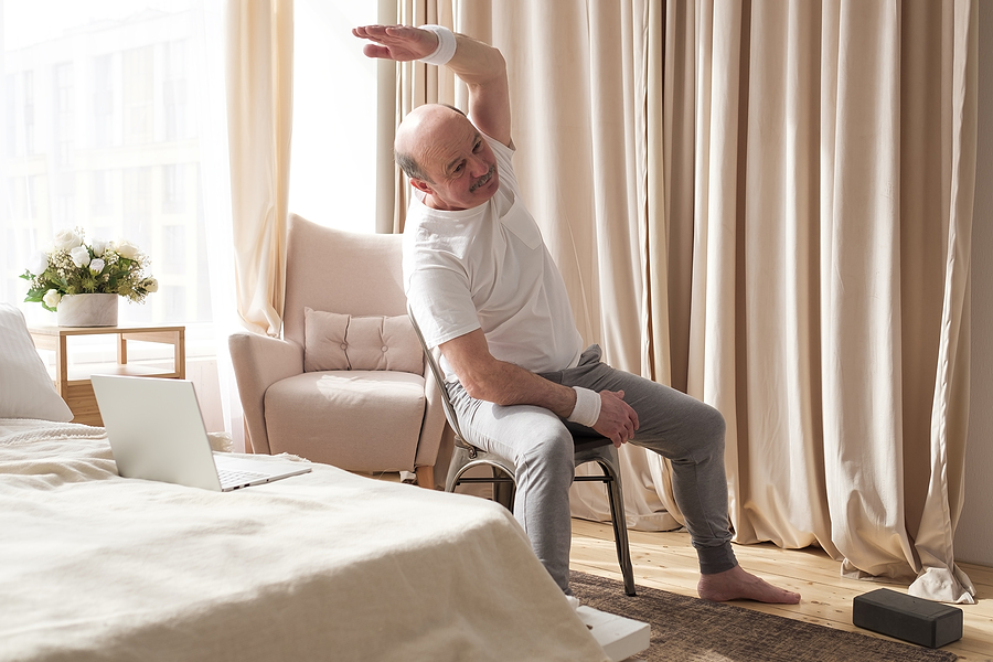 A senior man does a seated chair stretch.