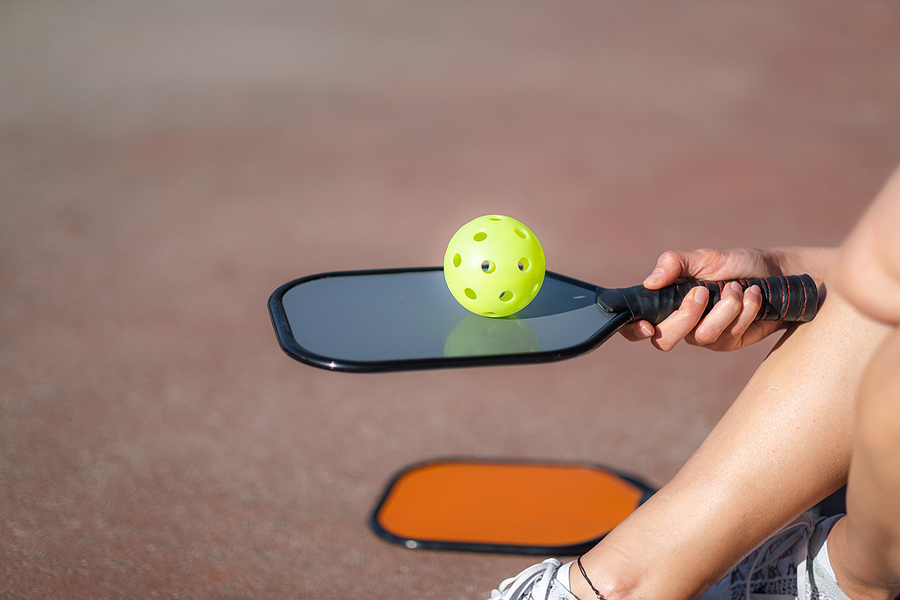 A woman holds a pickleball paddle and ball.