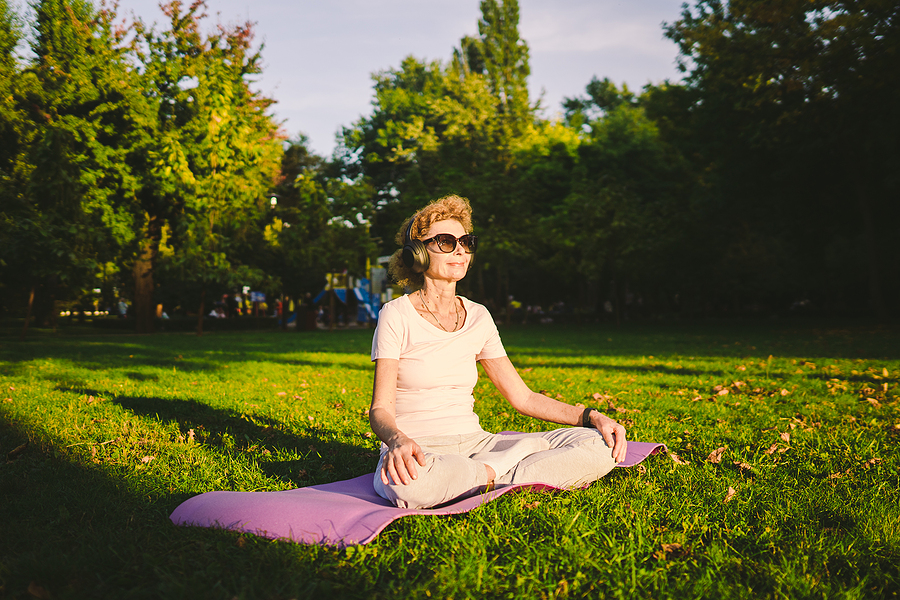 Senior woman sitting on a yoga mat with headphones at the park
