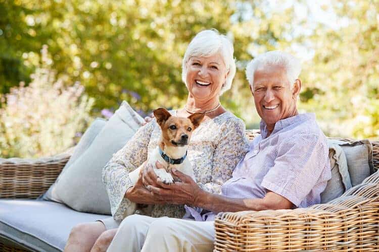 A senior couple smiling happily on outdoor seating with their dog.