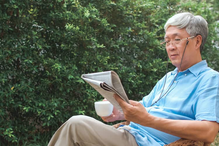 A senior man enjoying the outdoors during the summer while reading the news.