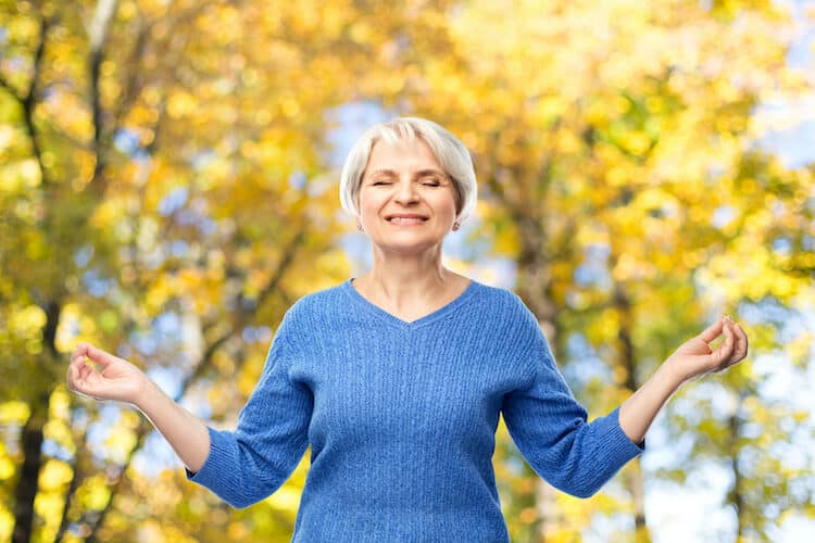 A senior woman in the autumn foliage reflecting on her spiritual wellness.