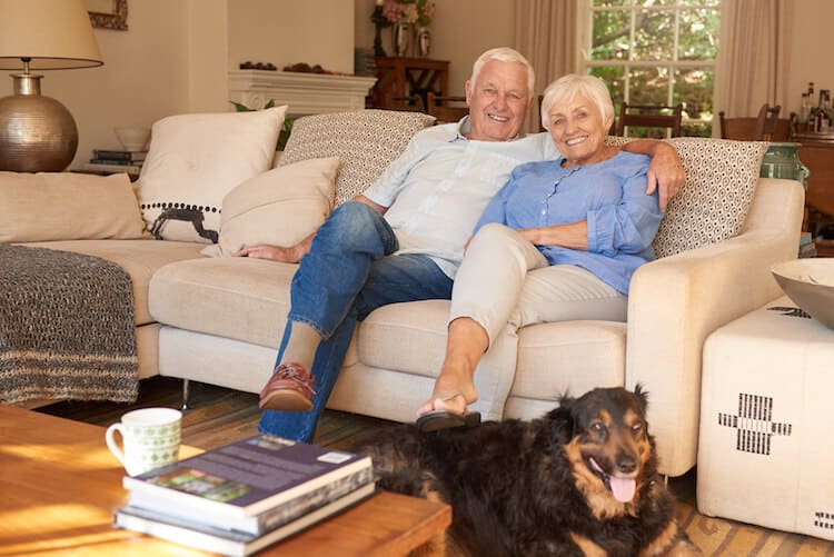 Seniro couple in their home with their pet dog sitting at their feet.