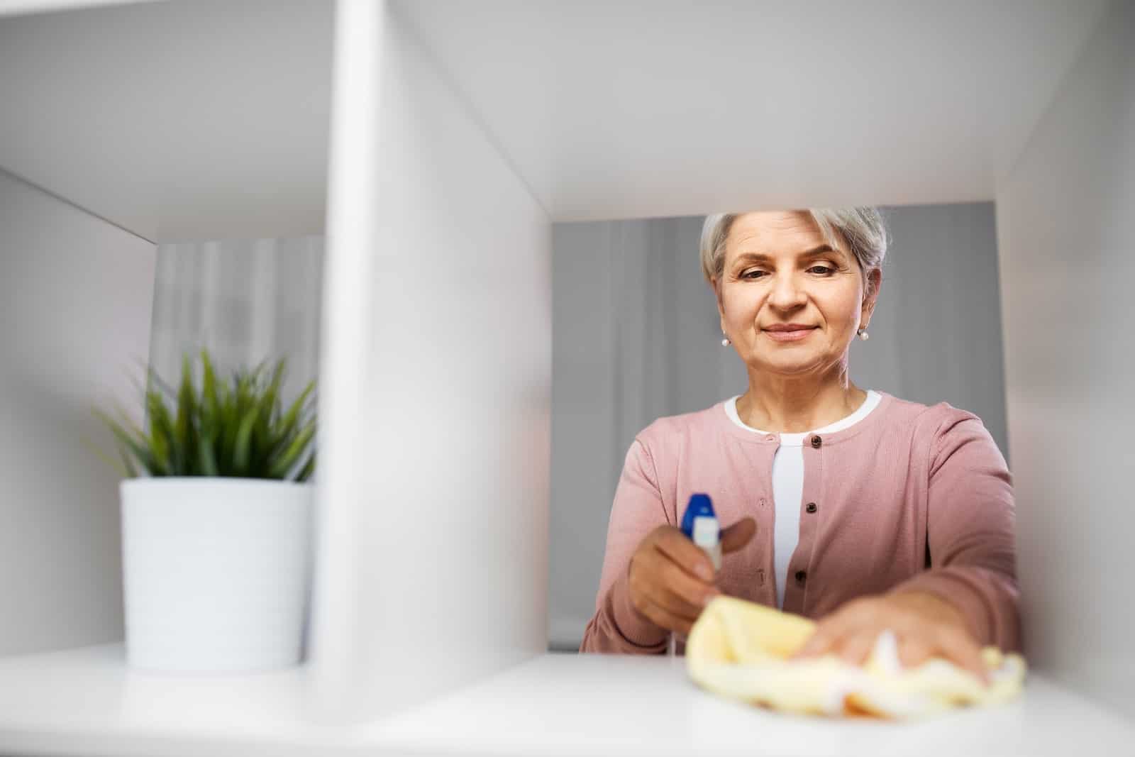 Older adult woman cleaning a shelving unit during spring cleaning.