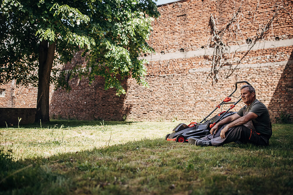 older man sitting on lawn next to lawn mower