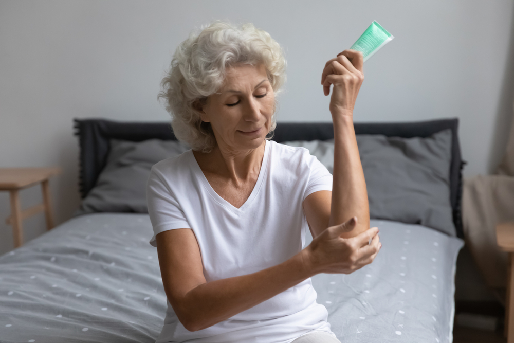 A senior woman puts ointment on her elbow to combat arthritis pain
