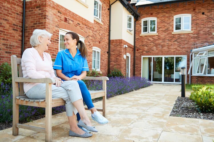 Senior woman talking to nurse outside on a bench. 