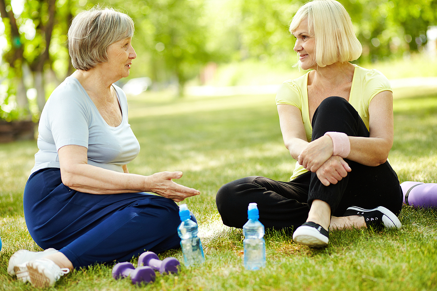 Two senior women are sitting on the lawn after a workout